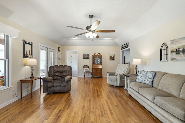 living area with baseboards, lofted ceiling, light wood finished floors, and ceiling fan