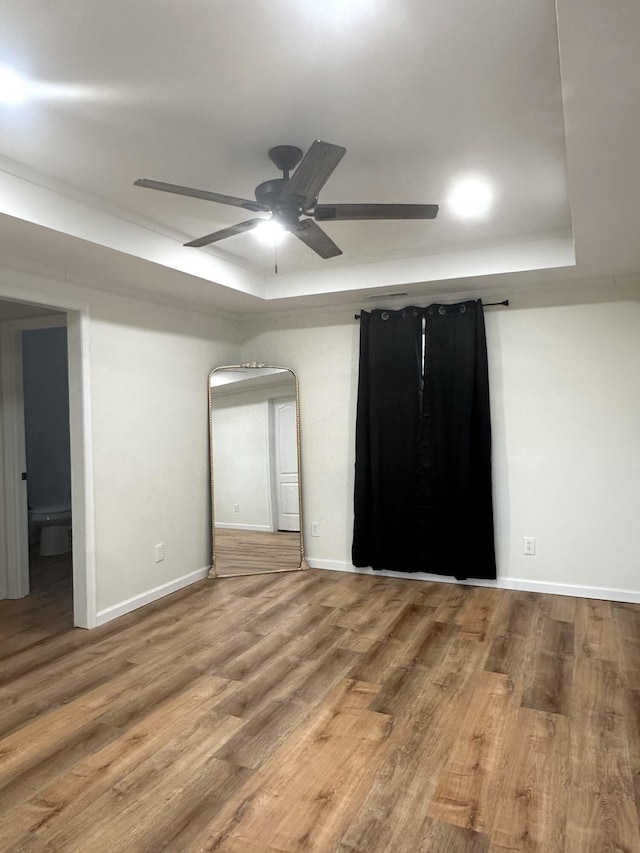 unfurnished room featuring a raised ceiling, wood-type flooring, and ceiling fan