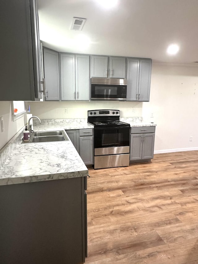 kitchen with stainless steel appliances, sink, light hardwood / wood-style flooring, and gray cabinetry