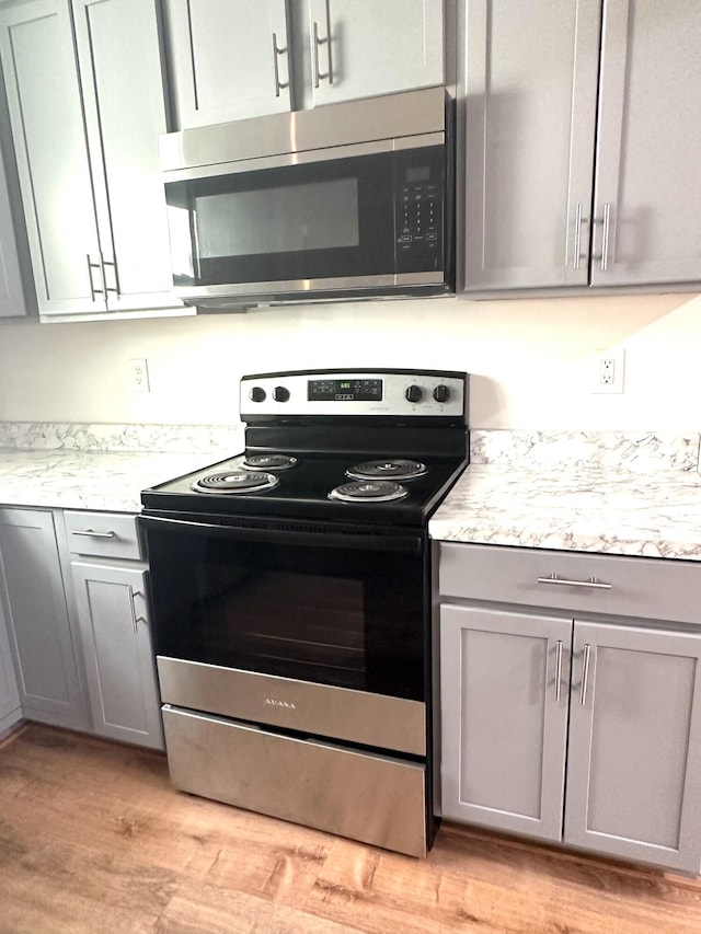 kitchen with stainless steel appliances, gray cabinets, light stone counters, and light wood-type flooring