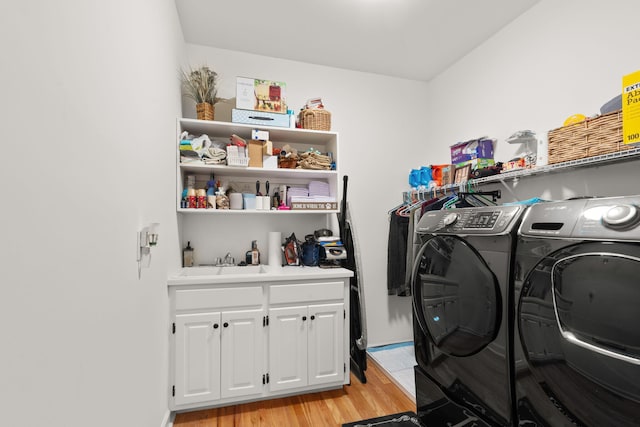 washroom featuring sink, light hardwood / wood-style flooring, washing machine and dryer, and cabinets