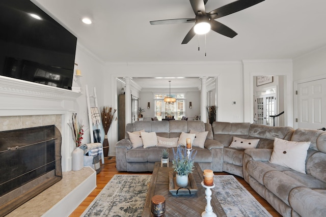 living room featuring a tiled fireplace, ornamental molding, ceiling fan, and light hardwood / wood-style floors