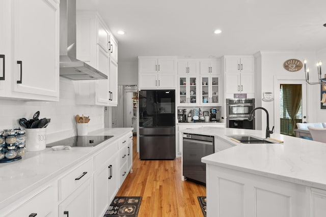 kitchen featuring decorative light fixtures, white cabinets, black appliances, light wood-type flooring, and wall chimney exhaust hood