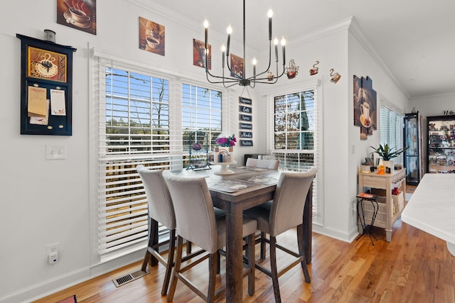 dining space with a notable chandelier, ornamental molding, and light hardwood / wood-style floors