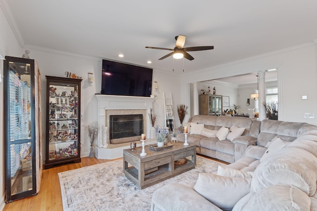 living room featuring ceiling fan, ornamental molding, a tiled fireplace, and light wood-type flooring