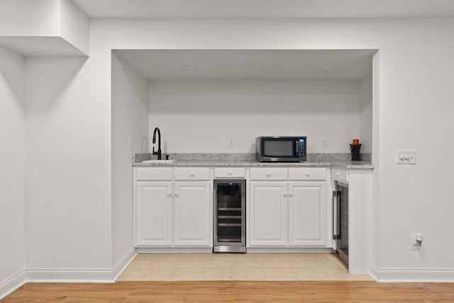 kitchen with sink, light hardwood / wood-style flooring, white cabinetry, wine cooler, and light stone counters