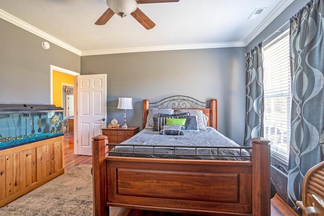 bedroom with wood-type flooring, a textured ceiling, ceiling fan, and ornamental molding