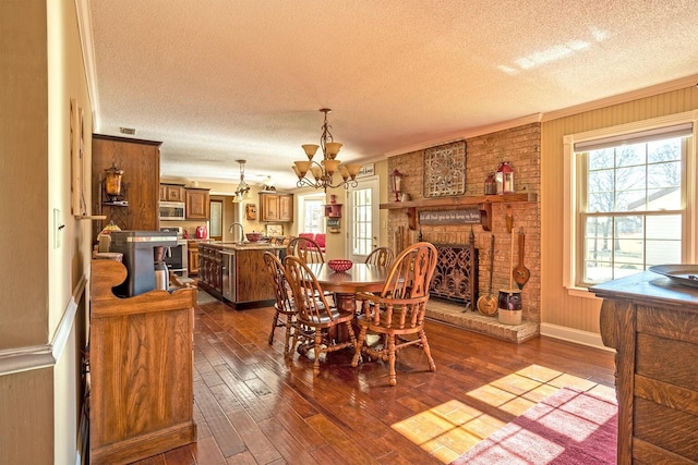 dining space featuring a brick fireplace, a textured ceiling, crown molding, a notable chandelier, and dark hardwood / wood-style floors