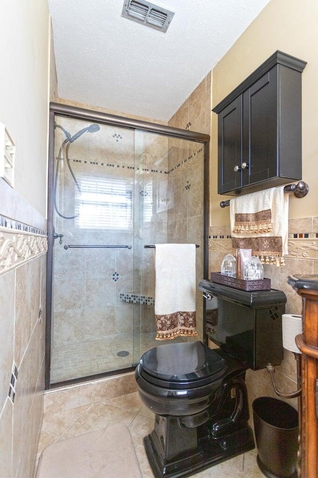 bathroom with tile patterned flooring, a textured ceiling, toilet, a shower with door, and tile walls