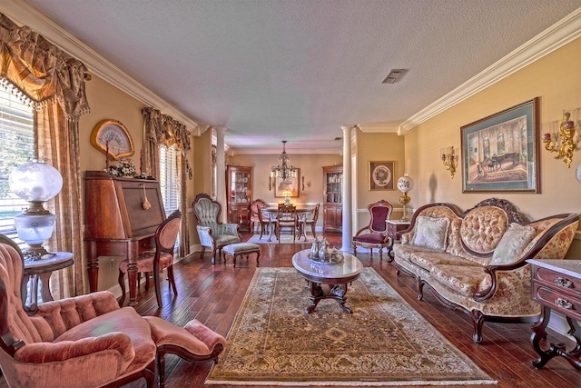 living room featuring dark wood-type flooring, an inviting chandelier, ornamental molding, a textured ceiling, and decorative columns