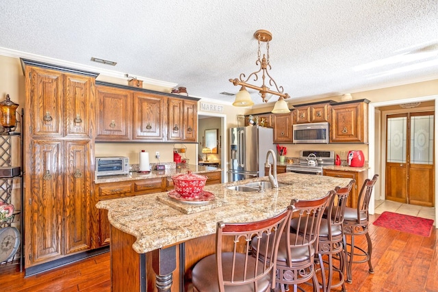 kitchen featuring a kitchen island with sink, sink, a textured ceiling, dark hardwood / wood-style flooring, and stainless steel appliances