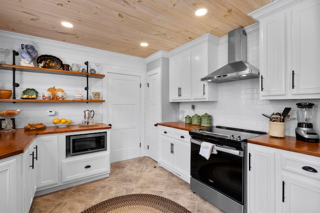 kitchen with white cabinets, wall chimney range hood, appliances with stainless steel finishes, tasteful backsplash, and butcher block countertops