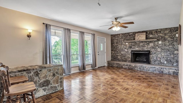 living room with parquet floors, a stone fireplace, and ceiling fan