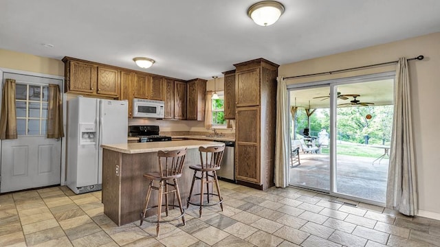 kitchen featuring a breakfast bar, a center island, a healthy amount of sunlight, and white appliances