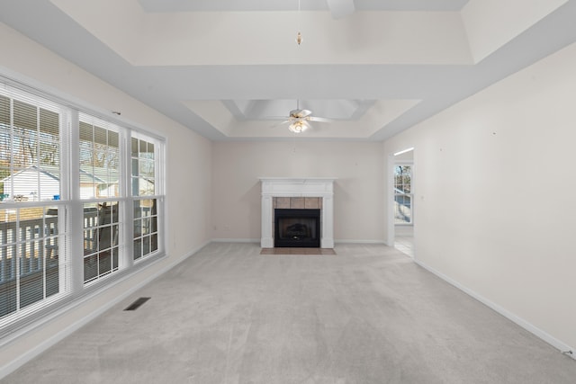 unfurnished living room with ceiling fan, a healthy amount of sunlight, light colored carpet, and a tray ceiling