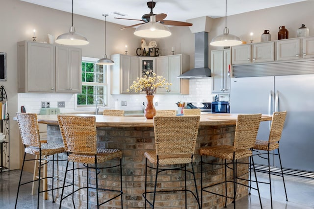 kitchen featuring wall chimney range hood, hanging light fixtures, and tasteful backsplash