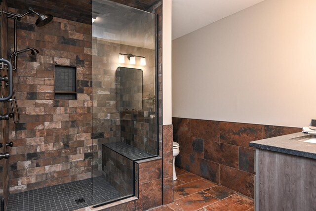 bathroom with vanity, toilet, tiled shower, and tile walls