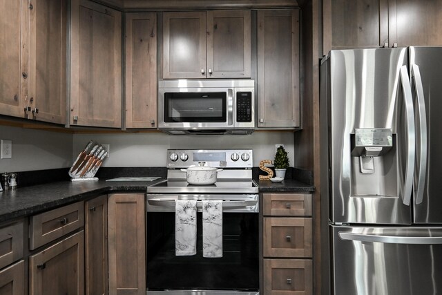 kitchen with dark brown cabinets, dark stone countertops, and stainless steel appliances