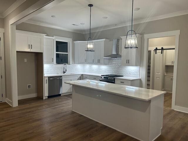 kitchen featuring a barn door, wall chimney range hood, white cabinetry, and appliances with stainless steel finishes