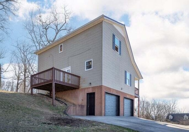 view of property exterior with a garage, driveway, a deck, and brick siding