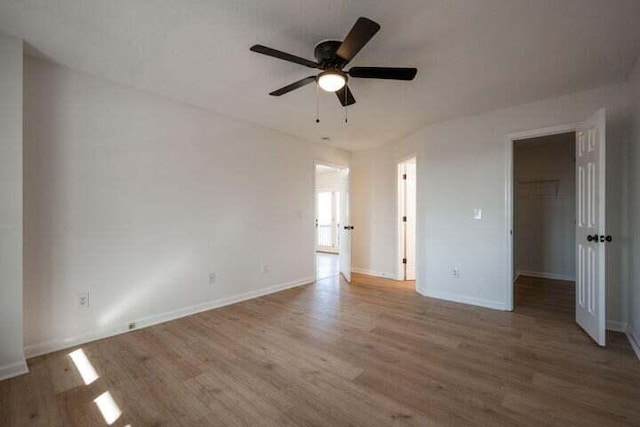 unfurnished bedroom with a walk in closet, a closet, ceiling fan, wood finished floors, and baseboards