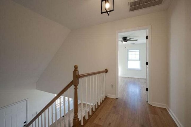 corridor featuring baseboards, visible vents, wood finished floors, and an upstairs landing