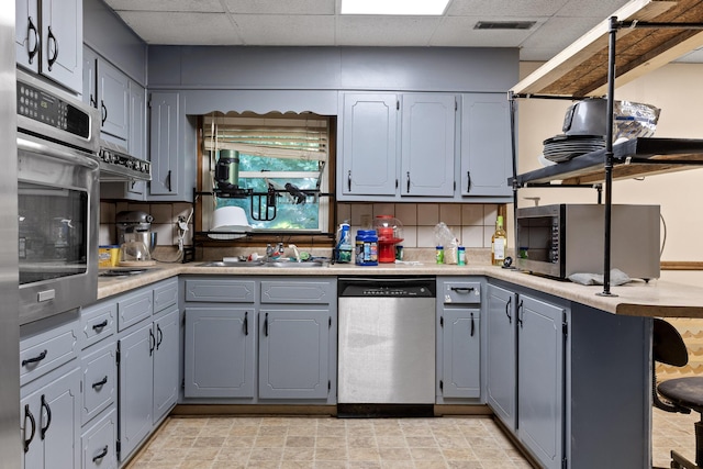 kitchen featuring gray cabinetry, backsplash, kitchen peninsula, a paneled ceiling, and appliances with stainless steel finishes