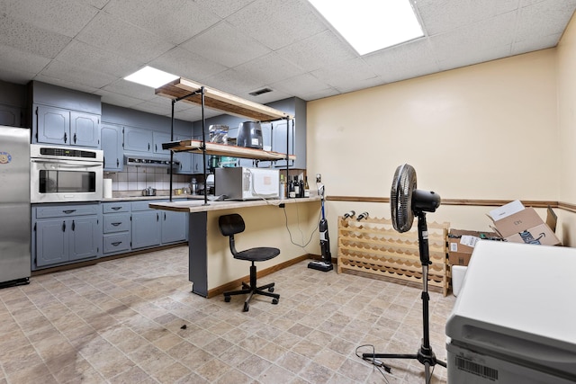 kitchen featuring a drop ceiling, backsplash, kitchen peninsula, a breakfast bar, and appliances with stainless steel finishes