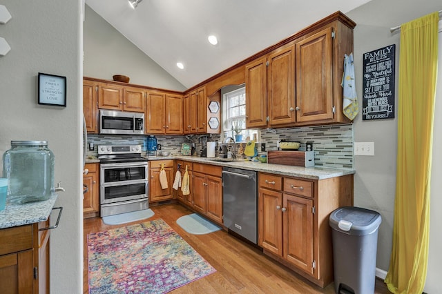 kitchen featuring lofted ceiling, appliances with stainless steel finishes, brown cabinets, light wood-style floors, and a sink