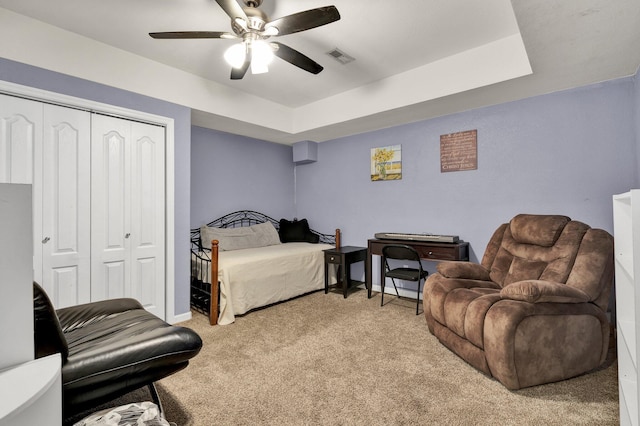 bedroom with a tray ceiling, a closet, light colored carpet, visible vents, and ceiling fan