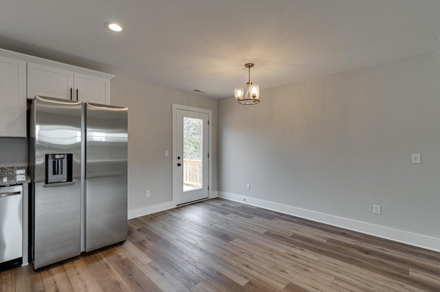 kitchen featuring stone countertops, white cabinetry, wood-type flooring, a chandelier, and stainless steel appliances