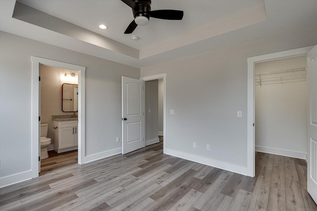 unfurnished bedroom featuring a closet, a walk in closet, light hardwood / wood-style flooring, and a raised ceiling