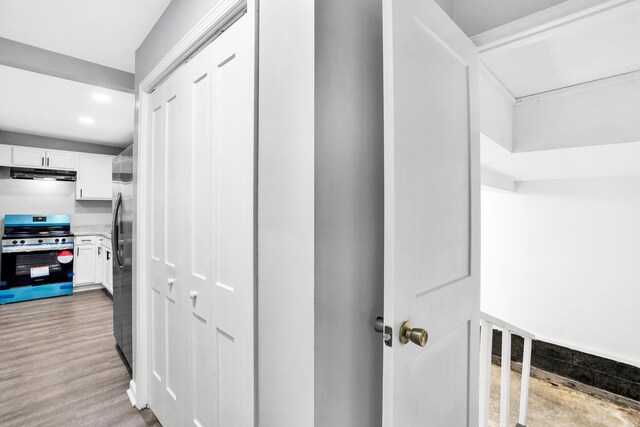 interior space featuring white cabinets, ventilation hood, light wood-type flooring, and stainless steel appliances