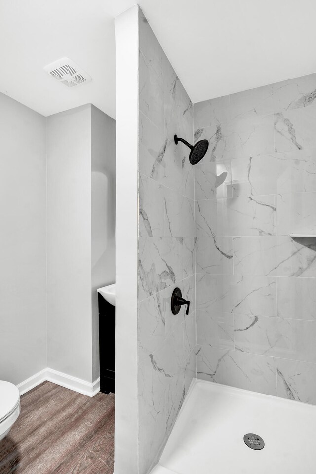 bathroom featuring tiled shower, wood-type flooring, and toilet