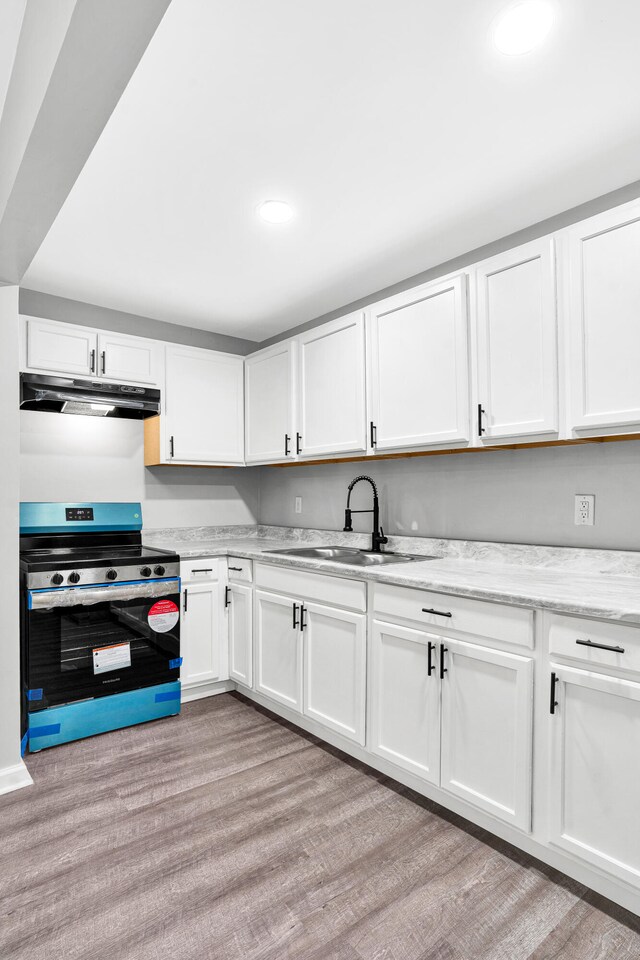 kitchen with white cabinets, sink, stainless steel range oven, light hardwood / wood-style flooring, and light stone counters