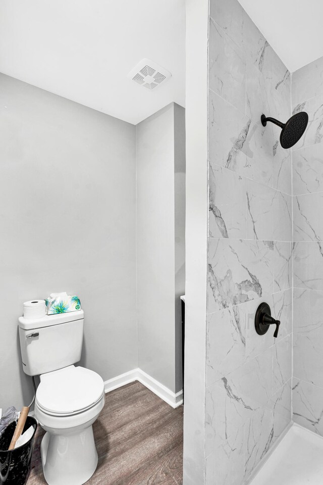 bathroom featuring a tile shower, wood-type flooring, and toilet