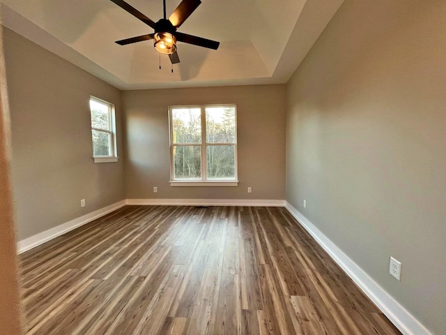 spare room featuring a raised ceiling, ceiling fan, and dark wood-type flooring