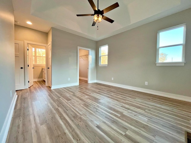 unfurnished bedroom featuring ensuite bath, ceiling fan, a spacious closet, multiple windows, and light hardwood / wood-style floors