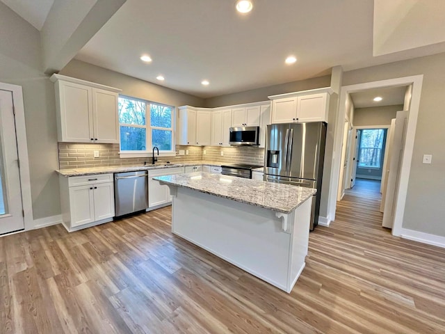 kitchen with appliances with stainless steel finishes, white cabinetry, a kitchen island, and sink