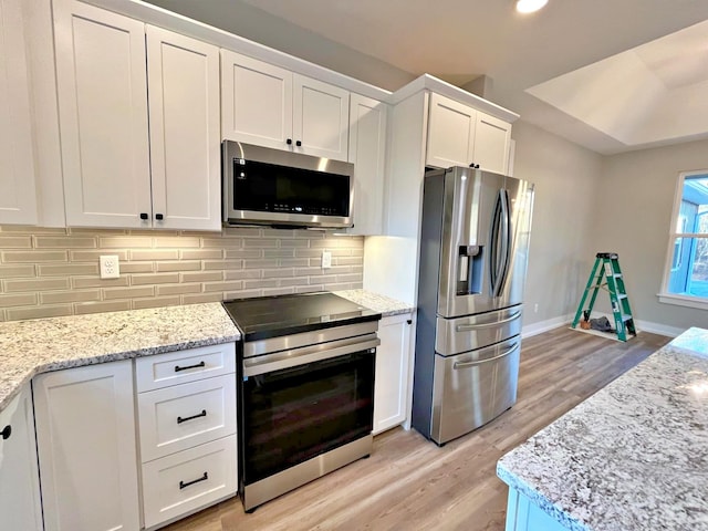 kitchen with light stone countertops, tasteful backsplash, appliances with stainless steel finishes, white cabinets, and light wood-type flooring