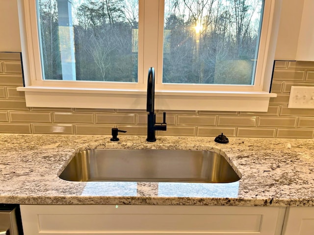 room details with tasteful backsplash, white cabinetry, sink, and light stone countertops