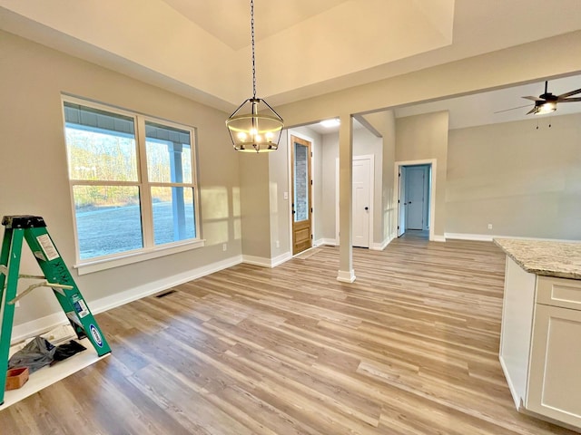 unfurnished dining area with ceiling fan with notable chandelier and light hardwood / wood-style floors