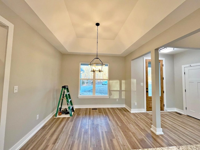 unfurnished dining area with a tray ceiling, hardwood / wood-style flooring, and an inviting chandelier