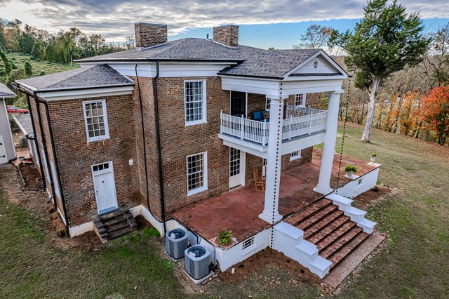 rear view of house with a patio, a balcony, central AC unit, and a lawn