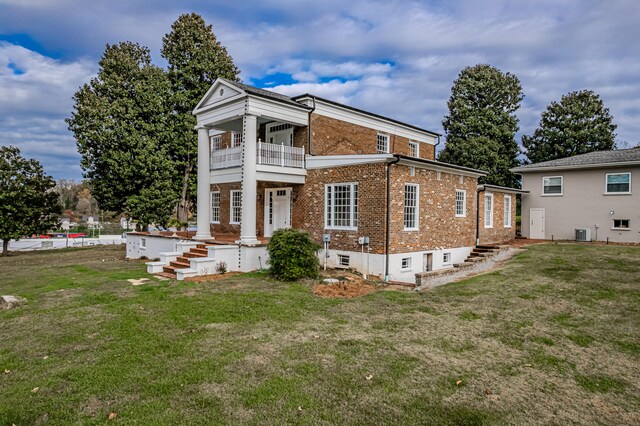 view of front of house with a balcony, central AC unit, and a front yard