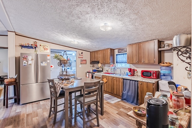 kitchen featuring lofted ceiling, sink, light hardwood / wood-style flooring, a textured ceiling, and stainless steel appliances