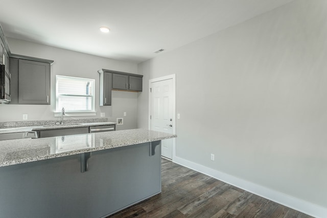 kitchen with light stone countertops, a kitchen breakfast bar, stainless steel appliances, sink, and dark hardwood / wood-style floors