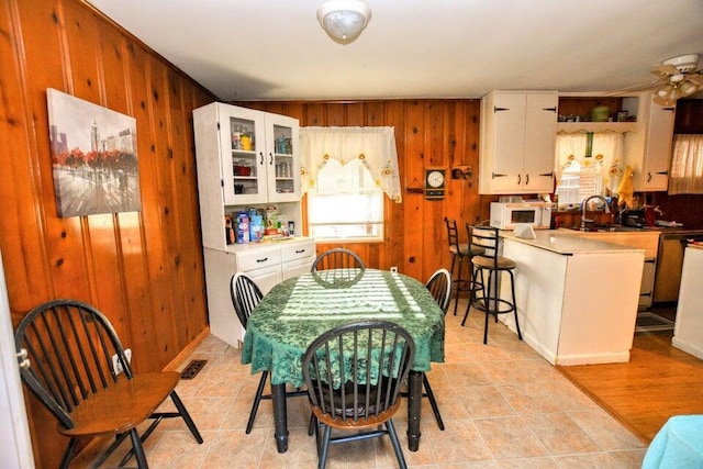 dining room with ceiling fan, sink, and wood walls