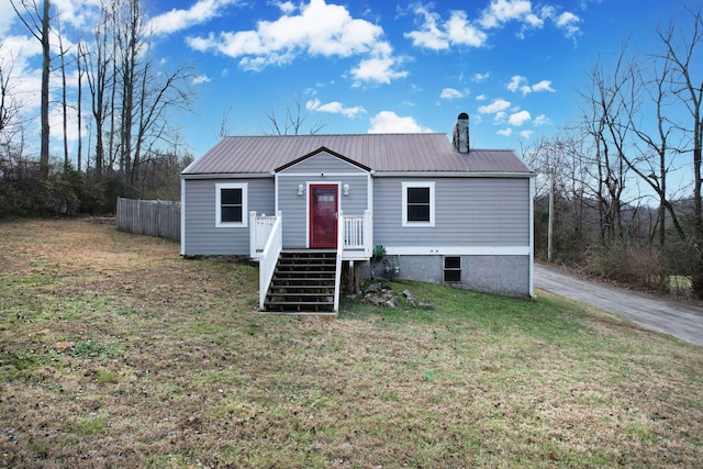 view of front of home with driveway, fence, a front yard, metal roof, and a chimney