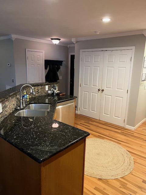 kitchen with dark stone countertops, crown molding, sink, and stainless steel dishwasher